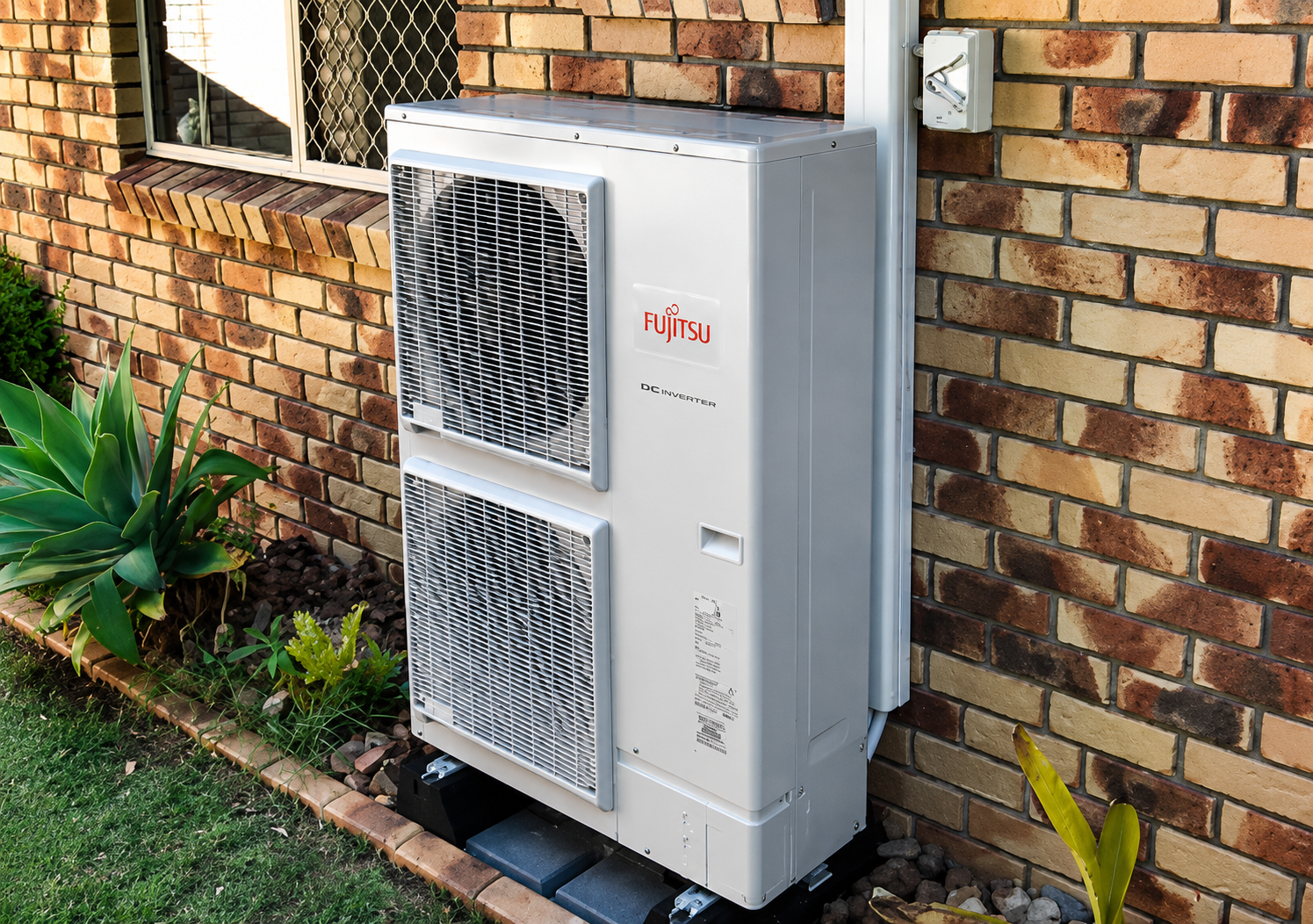 A Fujitsu reverse-cycle outdoor unit installed against a brick home by SETPOINT