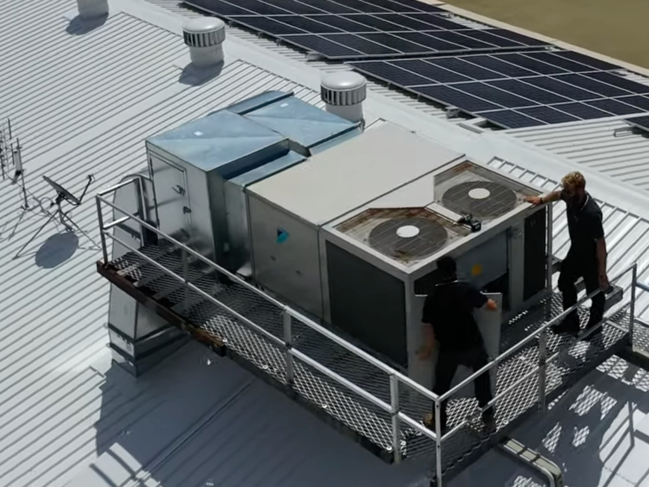 A rooftop packaged air conditioning unit being serviced by SETPOINT technicians, with rooftop solar behind